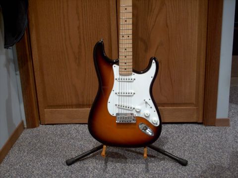 1986 Ford Bronco - A sunburst electric guitar is displayed on a stand in front of a wooden door.