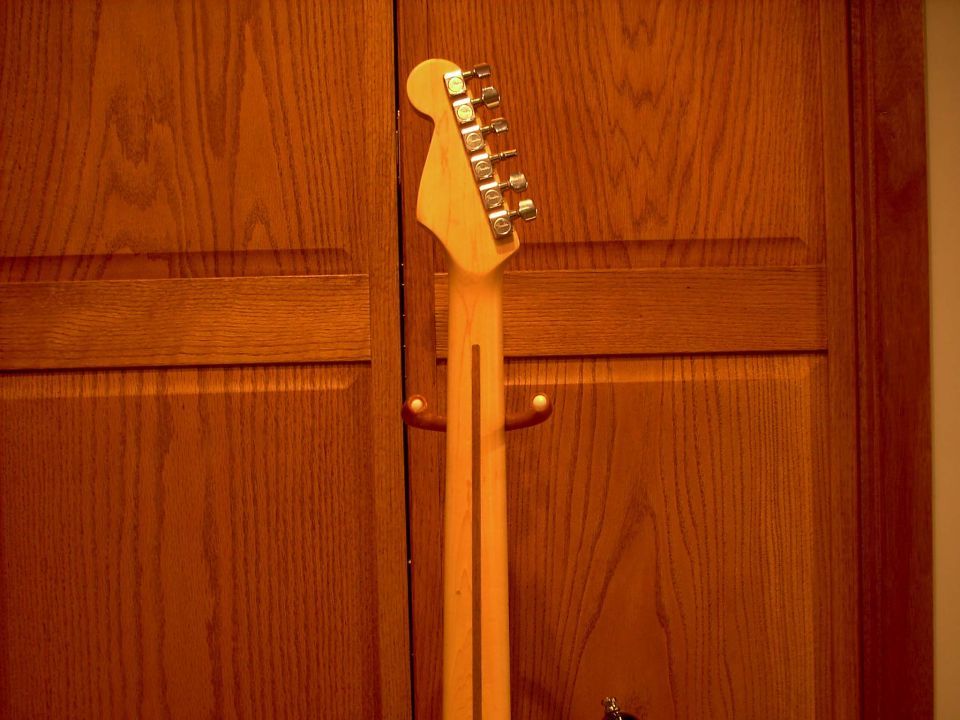 Guitar neck and headstock with tuning pegs against wood-paneled doors
