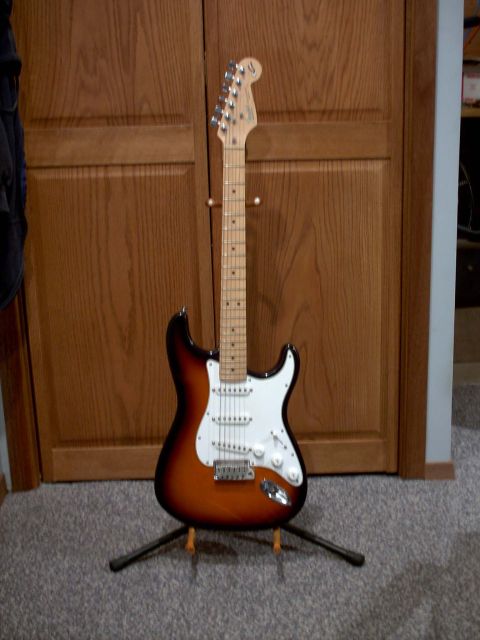 1986 Ford Bronco - An electric guitar with a sunburst finish stands on a display stand against a backdrop of closed wooden doors.