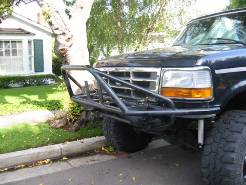 1992 Ford Bronco - Front three-quarter view of a lifted dark Ford truck wearing a bare-steel tubular front bumper with a grille guard and integrated winch mou…