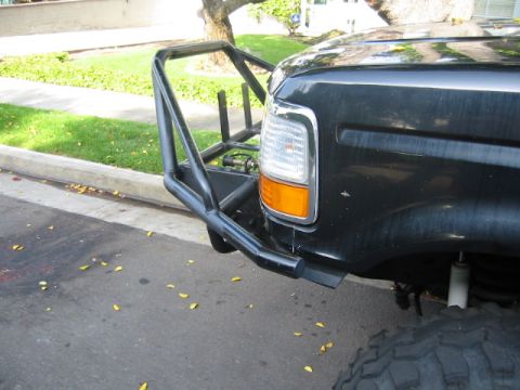 1992 Ford Bronco - Close-up of the passenger-side corner of a black Ford truck fitted with a fabricated tube front bumper with a raised light bar hoop and pre…