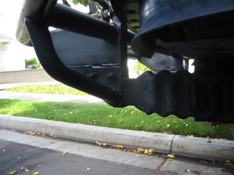 1992 Ford Bronco - Low-angle view under the front of a lifted truck showing the tube bumper's bolted mounting plate sandwiched to the frame horn, with the bla…