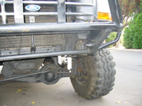 1992 Ford Bronco - Low-angle close-up of the front passenger corner of a white Ford truck fitted with a black tubular front bumper and grille guard, with the…