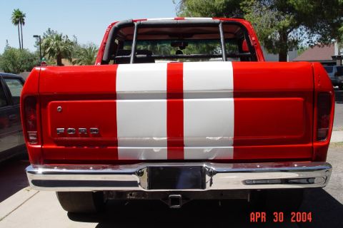 1979 Ford Bronco - Rear view of a red Ford pickup truck with bold white racing stripes and a chrome bumper.