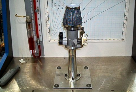 1985 Ford LTD Crown Victoria - A carburetor with an air filter is mounted on a stand next to a manometer with red fluid.