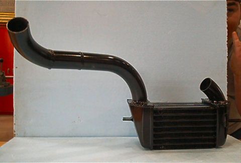 1985 Ford LTD Crown Victoria - A black intercooler pipe with a large radiator-like component is displayed against a light blue background.