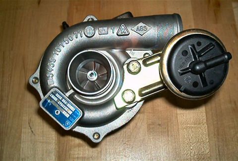 1985 Ford LTD Crown Victoria - A clean KKK/BorgWarner turbocharger sitting on a wooden floor, viewed into the compressor housing inlet with the aluminum compressor wheel…
