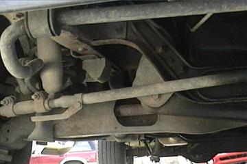 1989 Ford Bronco - Close-up view of the undercarriage, showing steering and suspension parts. Another vehicle is partially visible in the background.