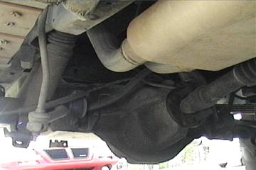 1989 Ford Bronco - Underside view of a vehicle's rear axle and exhaust system, with a partial view of another vehicle in the background.