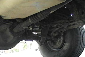 1989 Ford Bronco - A close-up view of the undercarriage of a vehicle, revealing mechanical parts and a tire.