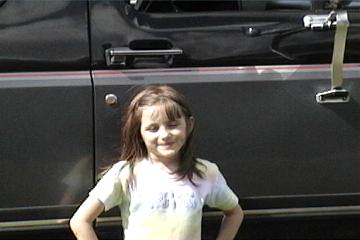 1989 Ford Bronco - A young girl stands in front of a dark-colored SUV.