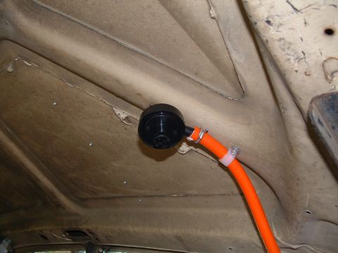 1979 Ford Bronco - Underside view of a tan-painted sheet-metal panel with a round black plastic grommet or vent fitting bolted through it, feeding a bright or…