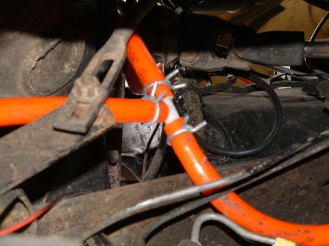 1979 Ford Bronco - Close-up under a vehicle showing bright orange hose routed through greasy, rusted chassis brackets and secured with white nylon clamps and…