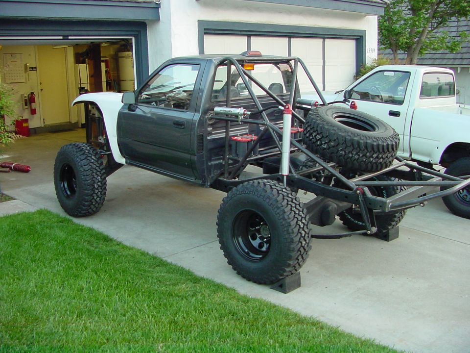 Tube-chassis mini truck buggy on huge mud tires and long-travel suspension parked on a driveway