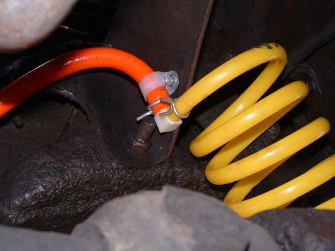 1979 Ford Bronco - Underbody close-up of a yellow powder-coated coil spring seated against a greasy axle housing, with an orange braided hose routed past it a…