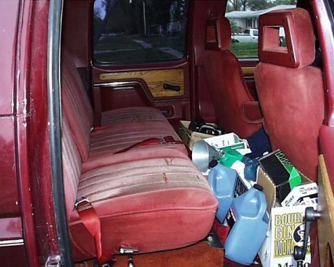 1988 Ford C-350 (Centurion Conversions) - The interior of a vehicle is filled with various items, including bottles of alcohol and cleaning supplies, behind the front seats.
