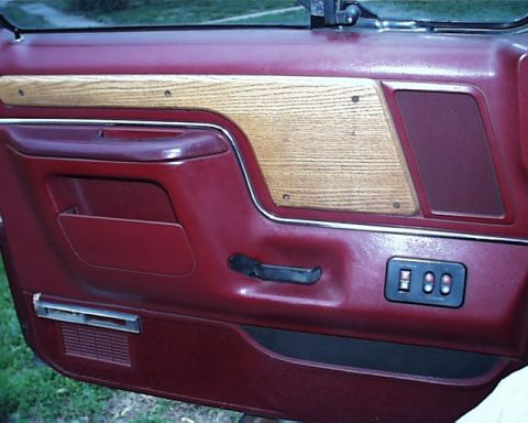 1988 Ford C-350 (Centurion Conversions) - Close-up of a vehicle's interior door panel, maroon upholstery and faux wood grain accents.