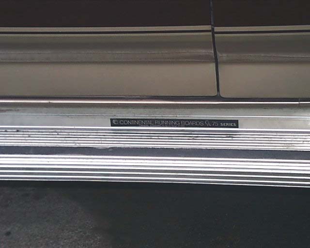 Polished aluminum Continental running board under a cream-colored rocker
