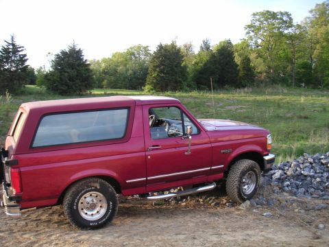 1994 Ford Bronco - This red Ford Bronco is parked on a dirt path next to a pile of rocks.