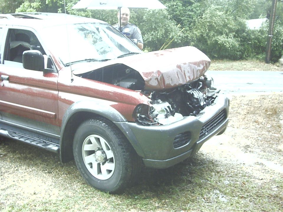 Maroon Mitsubishi Montero Sport SUV with front-end crash damage, hood buckled, parked on grass