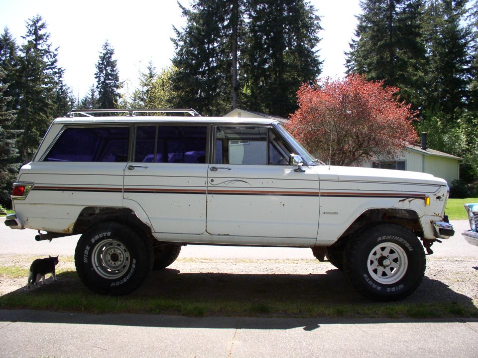 Lifted white full-size Jeep wagon with roof rack and white-letter tires in driveway