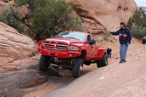 1978 Ford Bronco - A red Dodge Ram pickup truck is shown off-roading on a rocky trail with a person standing nearby.