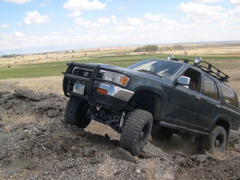 1978 Ford Bronco - A dark green SUV navigates a rocky incline under a partly cloudy sky.