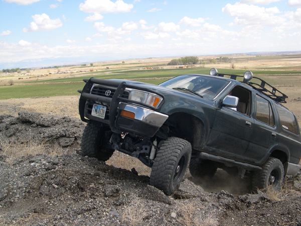 Dark green SUV with bull bar and roof rack driving on rocky terrain