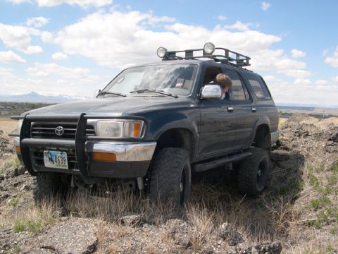 1978 Ford Bronco - Toyota 4Runner with off-road modifications navigates a rough, dry landscape under a cloudy sky.