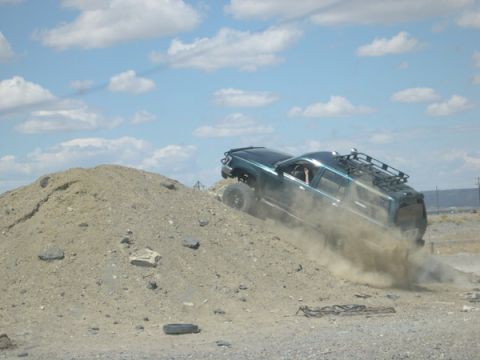 1978 Ford Bronco - A dark green SUV navigates a steep dirt incline, raising a cloud of dust.