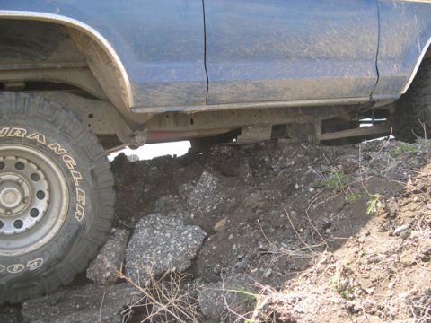 1978 Ford Bronco - The side view of a blue SUV shows its chassis and tire navigating over rough, rocky ground.