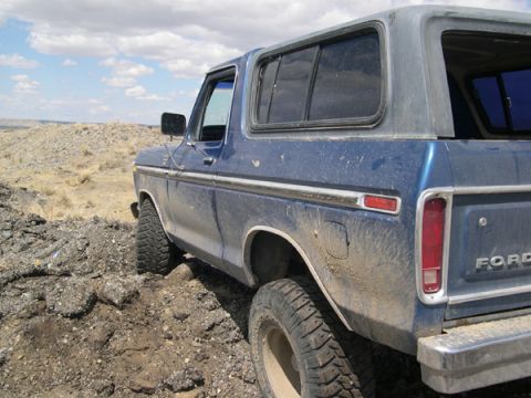 1978 Ford Bronco - A blue 1978 Ford Bronco navigates a rough, dusty terrain under a cloudy sky.