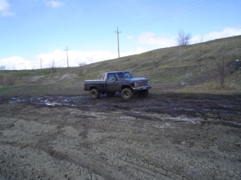 1981 Ford Bronco - Pickup truck navigates a challenging muddy terrain under a partly cloudy sky.