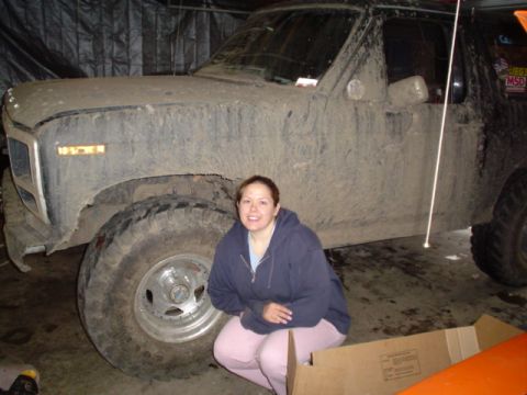Mud-covered 1981 Ford Bronco parked in a garage with a woman crouching in front of the tire