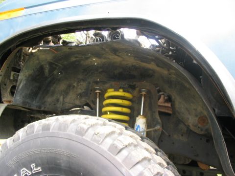 1986 Ford Bronco - The suspension system and wheel well of a vehicle are visible, with yellow coil springs and shock absorbers.