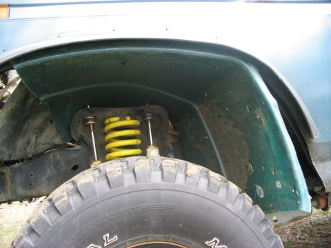 1986 Ford Bronco - Close-up of a vehicle's wheelwell shows a yellow coil spring and a large tire, suggesting an older model SUV.