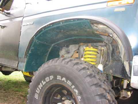 1986 Ford Bronco - The wheelwell of a green Ford Bronco shows modifications and a yellow shock absorber.