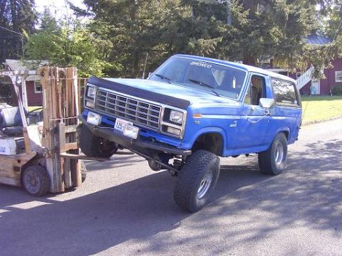 1980 Ford Bronco - A blue 1980 Ford Bronco is being lifted by a forklift on a paved surface.