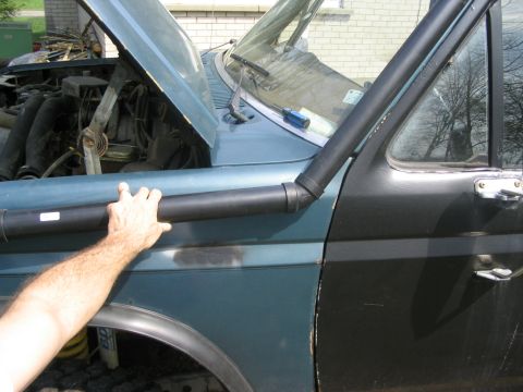 1986 Ford Bronco - A hand is shown on the snorkel of a teal and black SUV, with the hood open revealing the engine bay.