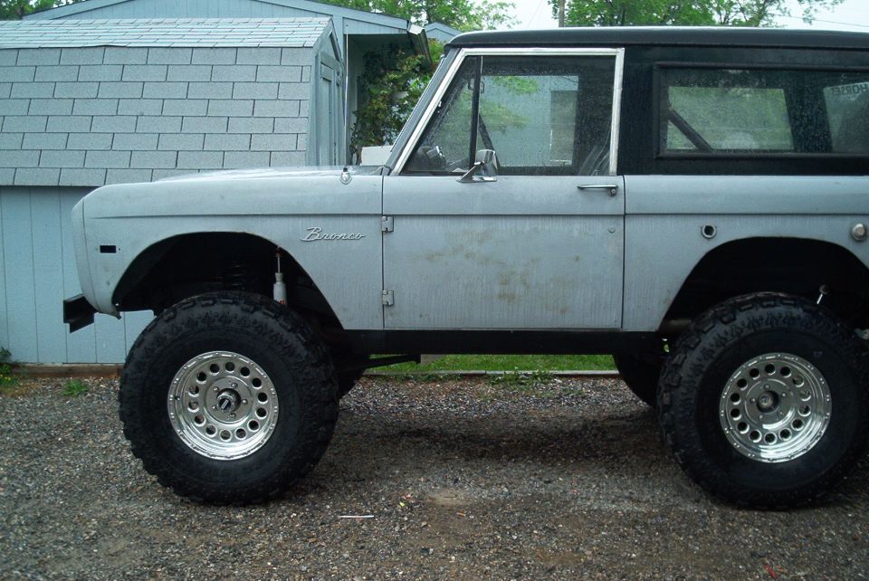 Side view of early Ford Bronco in primer gray with lift and chrome wheels
