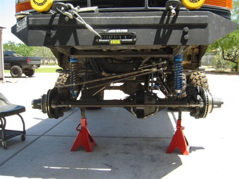 1994 Ford Bronco - The front suspension and undercarriage of a lifted vehicle are visible, supported by red jack stands, with another truck in the background.