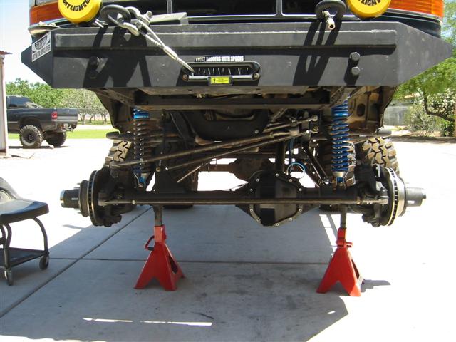 Underside front axle of a raised Bronco on red jack stands with coilover shocks