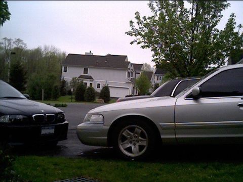2002 Ford Crown Victoria - A silver 2002 Ford Crown Victoria is parked next to a black car in front of a residential building.
