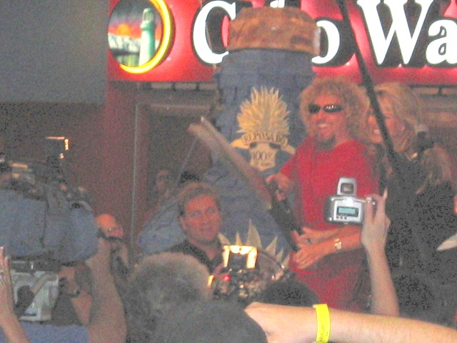 Crowd gathered around a man in a red shirt, with cameras and a sign that says "Cabo Wabo"