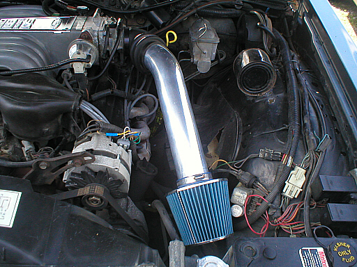 Engine bay showing an aftermarket cold air intake with a blue filter, alternator, and wiring. Supermotors.net logo visible