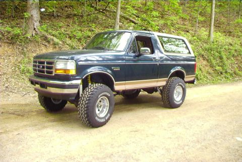 1995 Ford Bronco - 1995 Ford Bronco with lifted suspension and off-road tires on a dirt path.