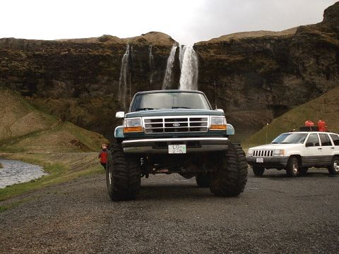 1996 Ford Bronco - A lifted green Ford Bronco is parked in front of a waterfall, with a white Jeep in the background.