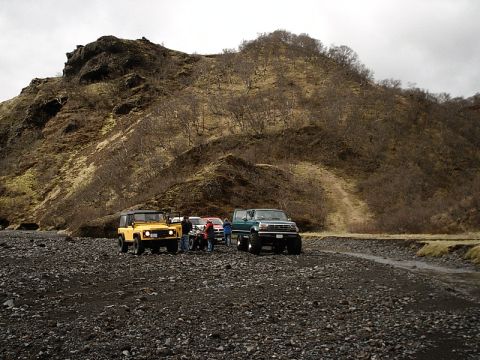 1996 Ford Bronco - Several off-road vehicles are stopped on a gravelly area near a hill.