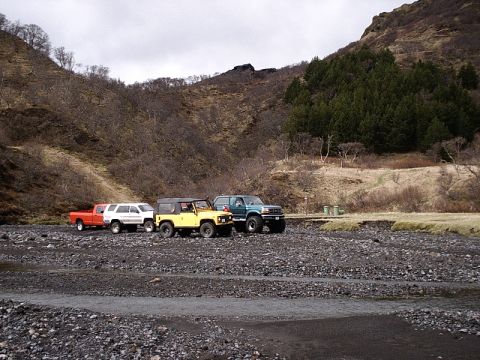 1996 Ford Bronco - A group of four-wheel drive vehicles are parked in a desolate, rocky area with a forested hill in the distance.