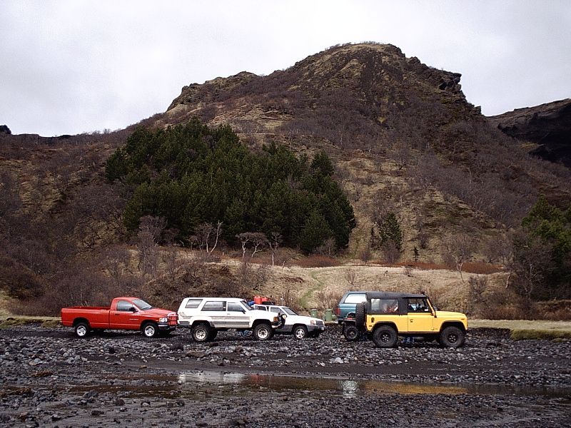 Four 4x4 vehicles parked on rocky riverbed below a mountain